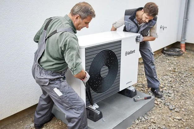 Zwei Techniker in Arbeitskleidung installieren eine Wärmepumpe vor einem Wohnhaus.