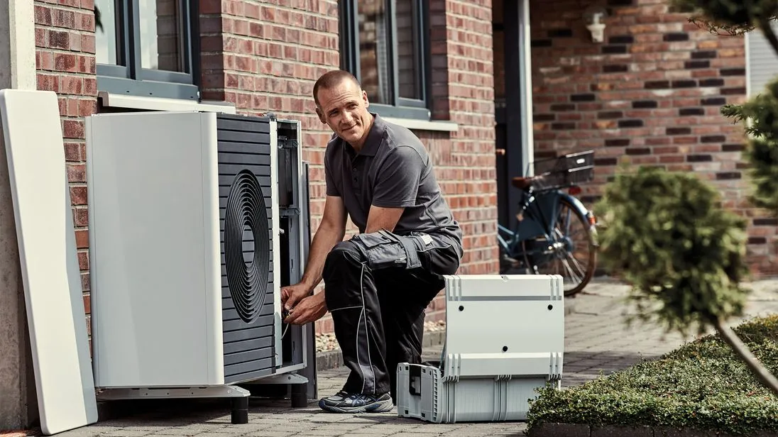 Ein Techniker installiert eine Wärmepumpe vor einem Wohnhaus.