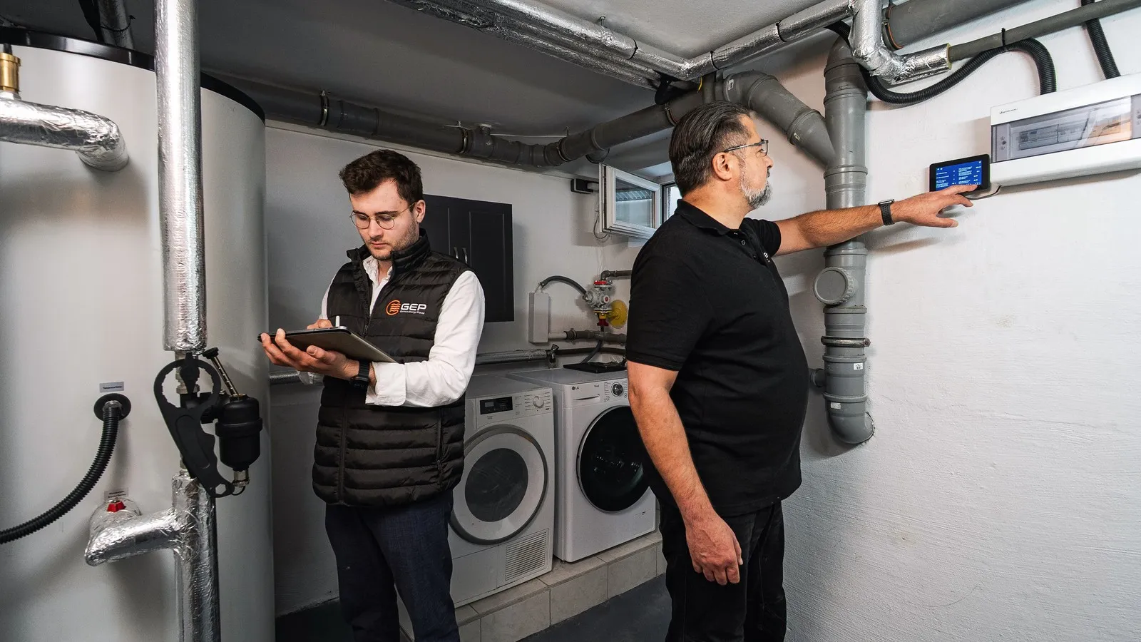 Zwei Techniker installieren eine Wärmepumpe im Keller eines Hauses. 