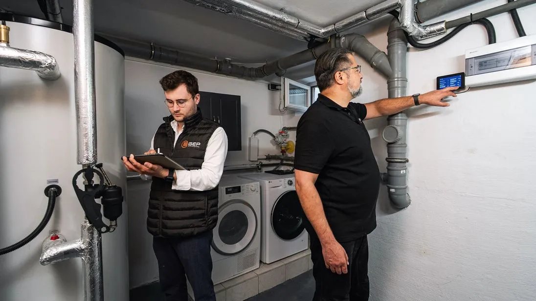Zwei Techniker installieren eine Wärmepumpe im Keller eines Hauses. 