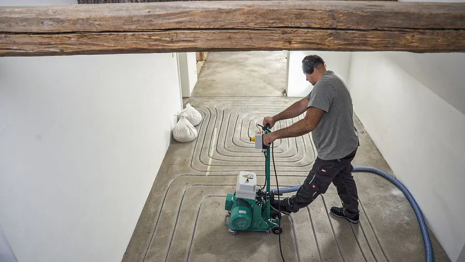 Ein Handwerker fräst die Leitungen für eine Fußbodenheizung. 