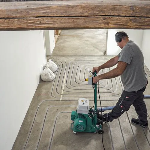 Ein Handwerker fräst die Leitungen für eine Fußbodenheizung. 