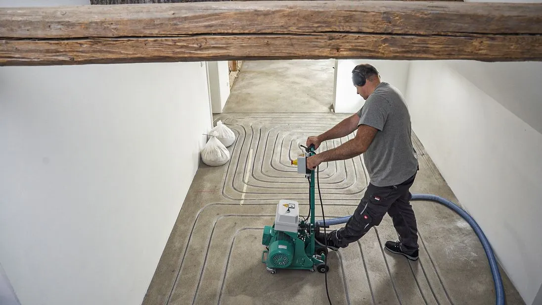 Ein Handwerker fräst die Leitungen für eine Fußbodenheizung. 