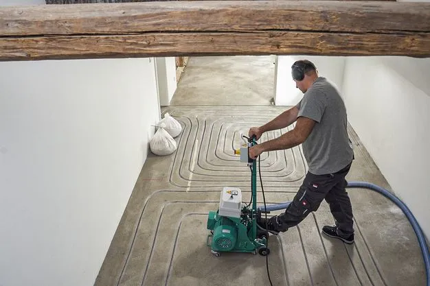 Ein Handwerker fräst die Leitungen für eine Fußbodenheizung. 