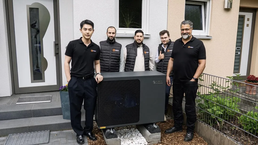 Eine Gruppe Männer der Firma GEP steht um eine schwarze Wärmepumpe herum. 