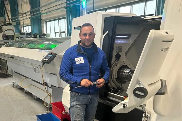 Ein Mann steht vor einer Maschine und hält ein Werkzeug in der Hand. 