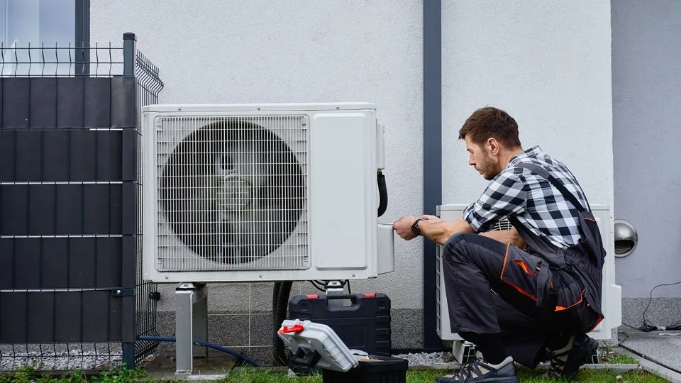 Ein Techniker installiert eine Wärmepumpe vor einem Wohnhaus.