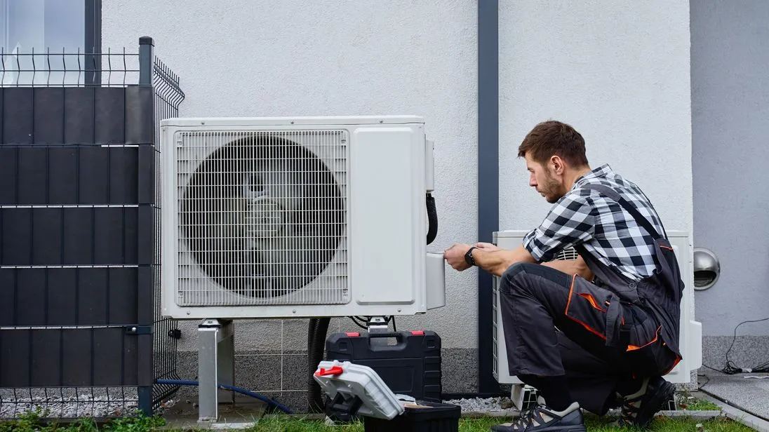 Ein Techniker installiert eine Wärmepumpe vor einem Wohnhaus.