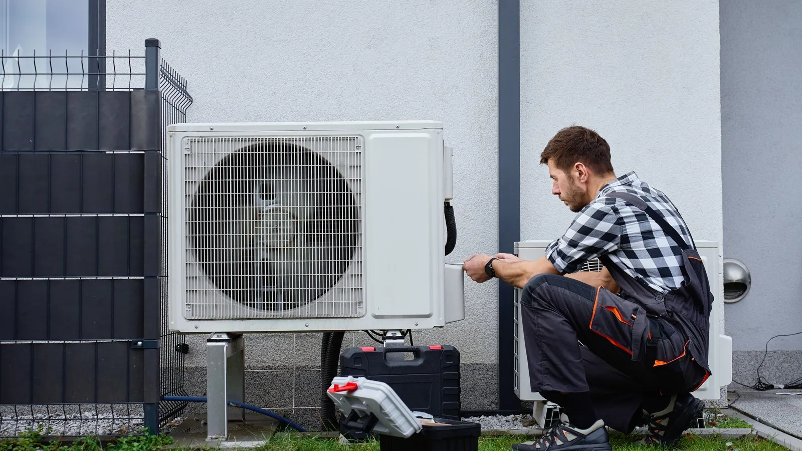 Ein Techniker installiert eine Wärmepumpe vor einem Wohnhaus.