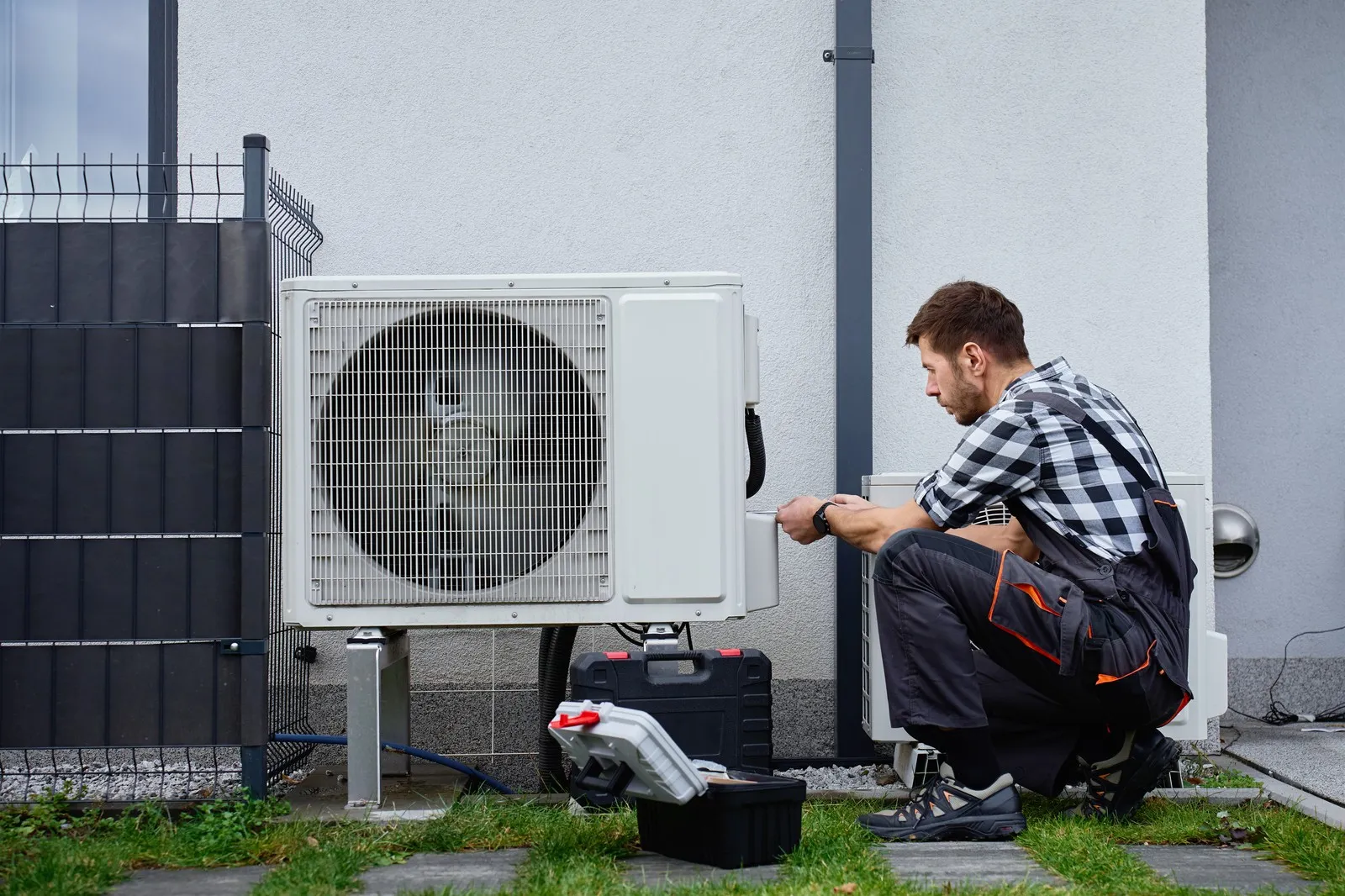 Ein Techniker installiert eine Wärmepumpe vor einem Wohnhaus.